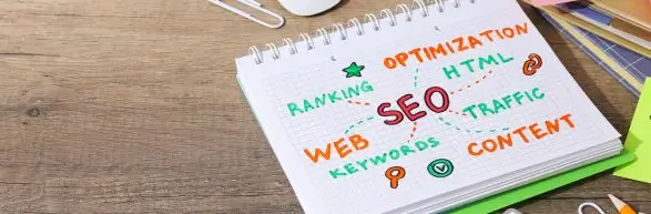 Otwarty notes na drewnianym biurku z kolorowo zapisanym schematem SEO. W centrum słowo ‘SEO’, od którego odchodzą powiązane hasła: ranking, optimization, HTML, traffic, content, keywords oraz web. Obraz symbolizuje złożoność pozycjonowania stron i potrzebę przemyślanej strategii SEO.