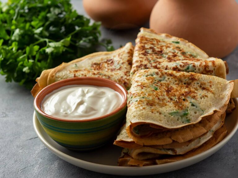 Naleśniki złożone w trójkąty na talerzu i sos w miseczce. Obrazek w artykule 4 przepisy na naleśniki na śniadanie w słodkiej i słonej wersji