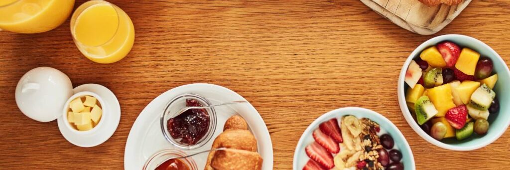 Stół z talerzykami i szklankami z sokiem, kawą, rogalikami, owocami. Obrazek w artykule Co na drugie śniadanie zazwyczaj jedzą gwiazdy?