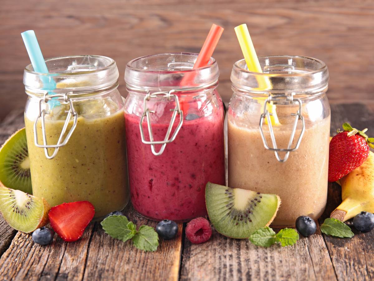 Trzy słoiki z smoothie w zielonym, buraczkowym i beżowym kolorze i owoce pokrojone na blacie. Obrazek w artykule 5 genialnych przepisów na smoothie na śniadanie, które dodadzą Ci witalności