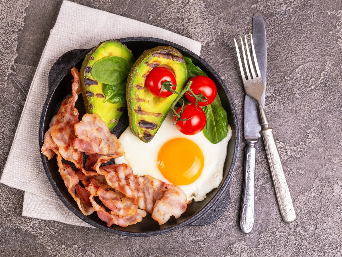 Talerz ze śniadaniem z jajek, bekonu, awokado zapiekanego i pomidorków. Obrazek w artykule TOP 4 pomysły na śniadanie białkowo tłuszczowe do pracy, które wzbudzi zazdrość innych pracowników