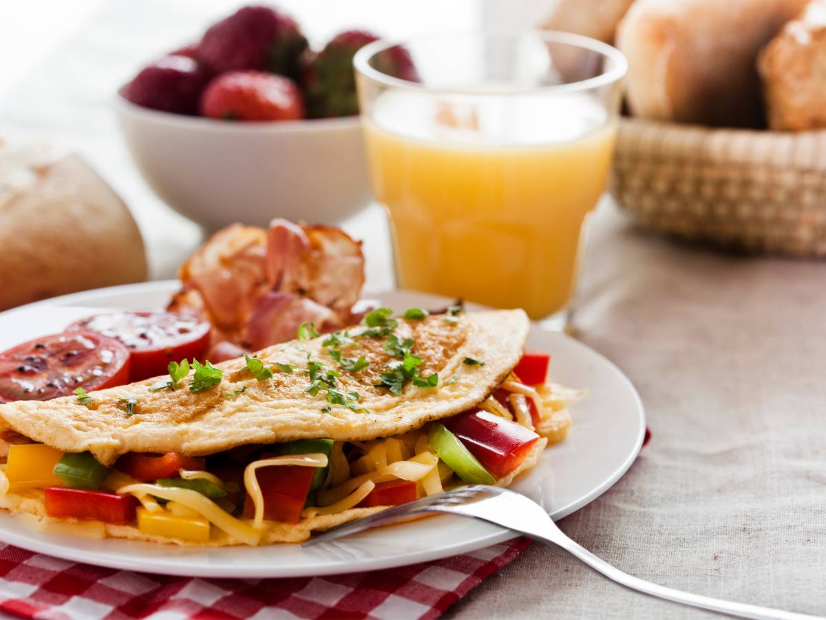 Talerz z omletem, szklanka soku i miseczka owoców. Obrazek w artykule 4 inspiracje na śniadanie do pracy bez chleba, jeśli masz dość kanapek