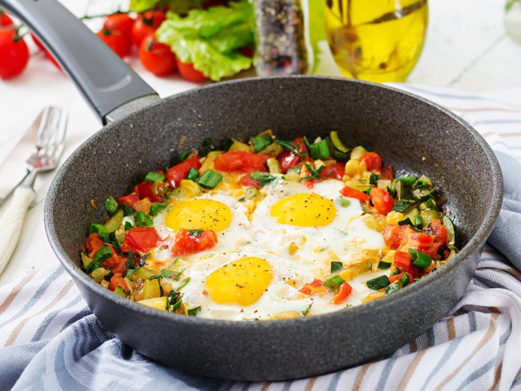 Jajka na pomidorach i szpinaku na patelni. Obrazek w artykule 5 pomysłów na pyszne śniadanie z jajkiem sadzonym, które zasmakuje Twoim domownikom
