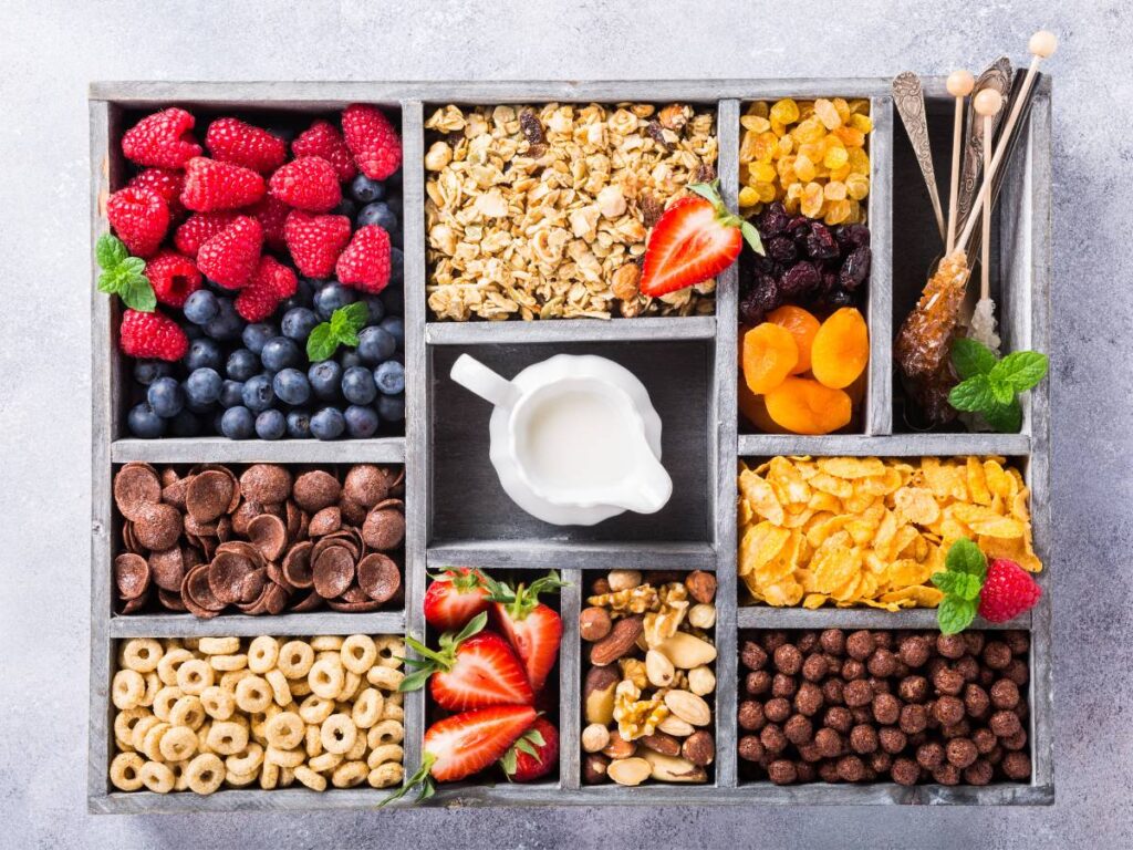 Pojemniki z dodatkami do jogurtu, który stoi po środku w dzbanku. Obrazek w artykule 4 inspiracje na szybkie śniadanie, gdy jesteś w biegu