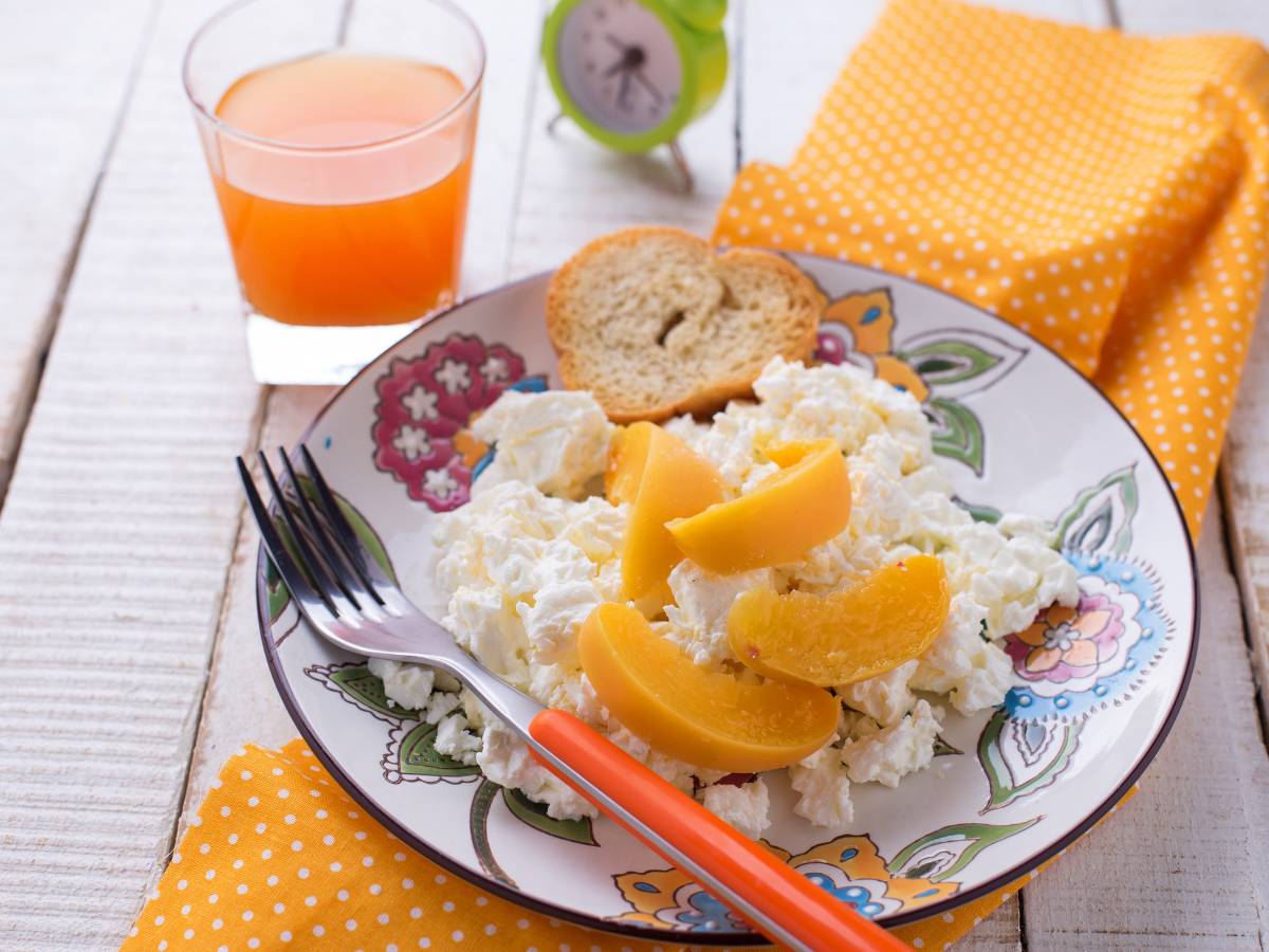 Talerz z twarogiem z brzoskwinia i mango i szklanka z sokiem. Obrazek w artykule Sposób na twaróg na śniadanie, który wpasuje się w każdą dietę i styl życia