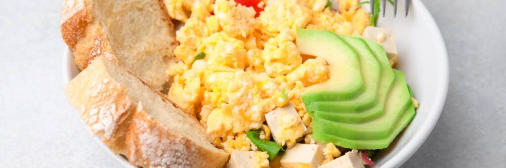 Talerz śniadania z jajecznicą, awokado, tofu i kromkami bagietki. Obrazek w artykule 5 pomysłów na wegetariańskie śniadanie z tofu, które zaskoczą Cię smakiem