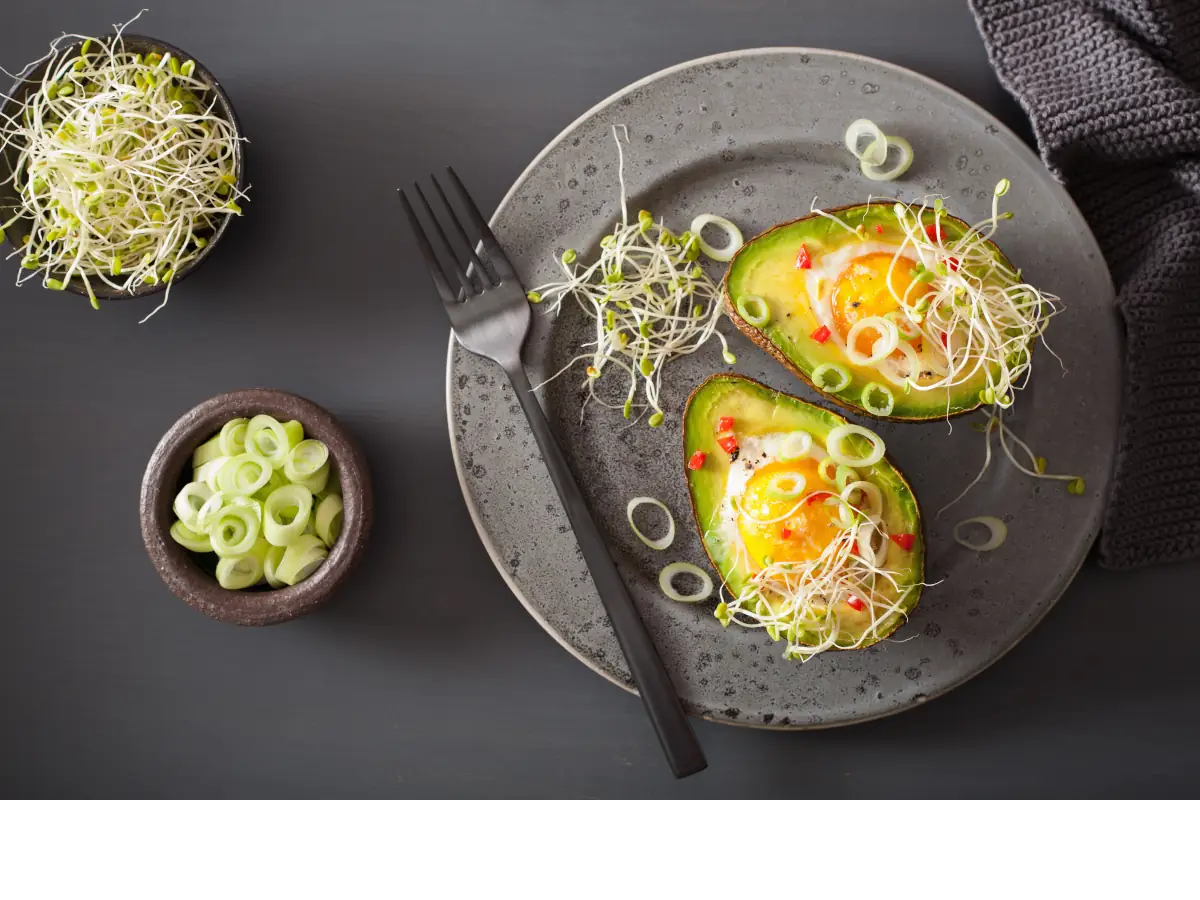 Jajka zapiekane w dwóch połówkach awokado. Obrazek w artykule 5 pomysłów na śniadanie z awokado, które Cię zachwycą