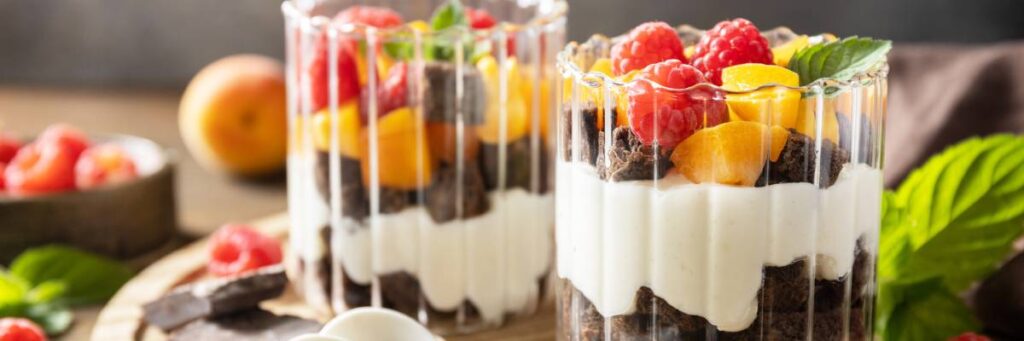 Szklanki z jogurtem i owocami przygotowane do jedzenia. Obrazek w artykule 4 inspiracje na fit śniadanie dla osób dbających o linię