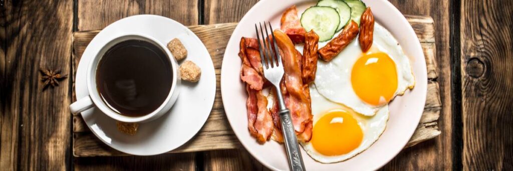 Talerz jajek sadzonych, bekon i parówki, obok filiżanka kawy. Obrazek w artykule 5 przepisów na parówki na śniadanie, które zaskoczą Twoją rodzinę