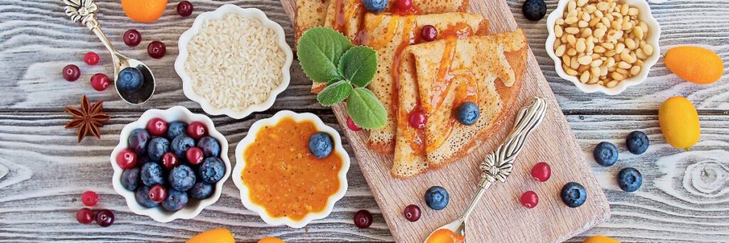 Dania sniadaniowe na stole: nalesniki, dżem , jogurt i inne. Obrazek w artykule TOP 3 przepisy na śniadanie, które zaskoczą Twoich bliskich