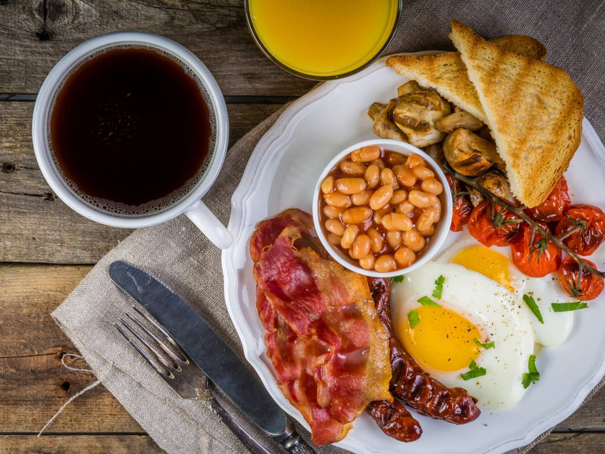 Brytyjskie śniadanie: czarna kawa w filiżance i talerz z jajkami, bekonem, kiełbaskami i fasolką. Obrazek w artykule Przepis na najlepsze śniadanie po angielsku - poczuj się jak w Londynie
