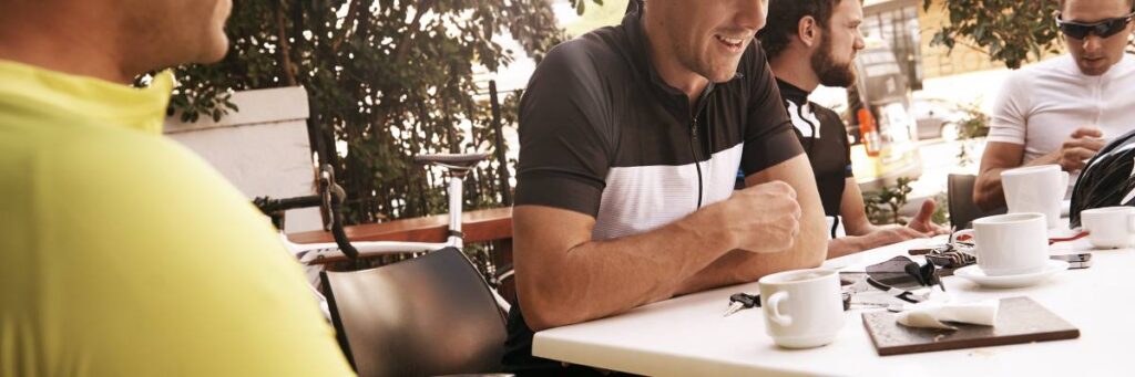 Biegacze siedzący na dworze przy stole. Obrazek w artykule Doradzamy, jak powinno wyglądać śniadanie przed treningiem, abyś dostrzegał efekty treningowe