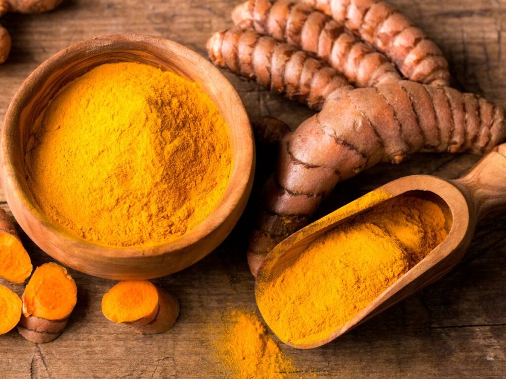 Drewniana miseczka i łopatka z mieloną kurkumą i korzenie obok.