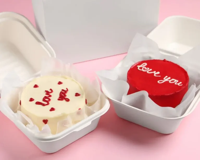 Dwa małe, ozdobne torciki z napisem „love you” zapakowane w nowoczesne, białe, biodegradowalne pudełka cukiernicze typu eko take-away, wyłożone papierem pergaminowym. Opakowania minimalistyczne, funkcjonalne i zgodne z trendami zrównoważonego rozwoju – przykład estetycznego i ekologicznego podejścia do pakowania deserów w 2025 roku.